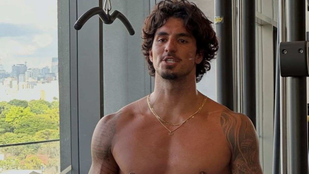Gabriel Medina, sem camisa, cabelo e barba, falando, em academia com fundo urbano.