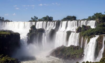 Vastas cataratas com quedas d'água brancas, rochas escuras, vegetação exuberante e céu azul.
