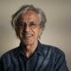 Caetano Veloso sorrindo, de óculos, com cabelo grisalho e camisa jeans.