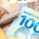 Cédulas de reais, com uma nota de R$100 'BANCO CENTRAL DO' e um maço amarrado.