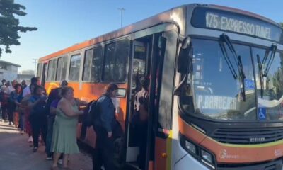 Muitos passageiros em fila para embarcar em um ônibus laranja com a rota '175 EXPRESSO TÚNEL'.