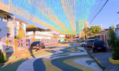Rua decorada com fitilhos, chão pintado, mural de jogador de futebol, bandeiras de países e carros.