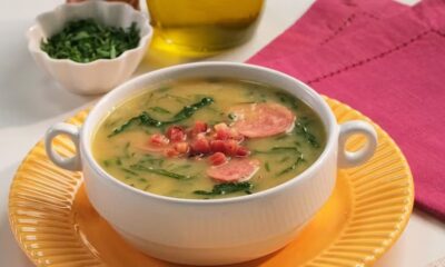 Uma tigela de caldo verde com linguiça, couve e pedaços de bacon, em um prato amarelo.