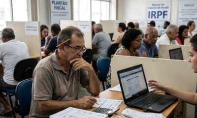 Pessoas em centro de atendimento fiscal preenchem documentos de Imposto de Renda com auxílio.