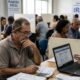 Pessoas em centro de atendimento fiscal preenchem documentos de Imposto de Renda com auxílio.