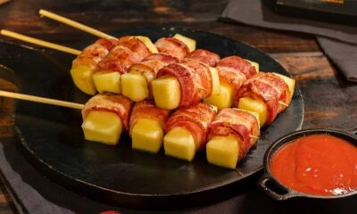 Espetos de queijo coalho envoltos em bacon dourado, servidos com molho vermelho.