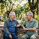 Dois homens idosos sorrindo em um banco de parque, conversando, com uma bengala.