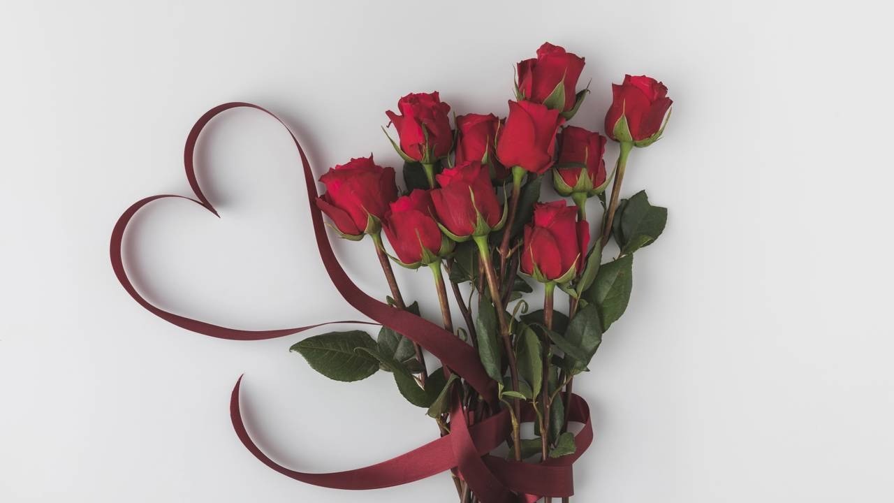 Buquê de rosas vermelhas com fita vermelha formando um coração em um fundo branco.