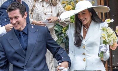 Dua Lipa e Callum Turner sorrindo de mãos dadas, com confete caindo sobre eles.