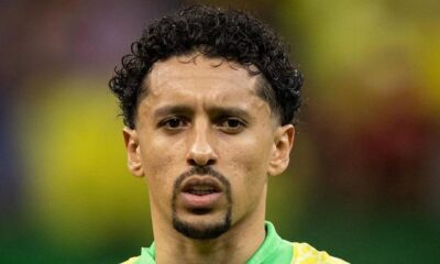 Marquinhos, jogador de futebol, com camisa verde e amarela, cabelo crespo e olhar sério.