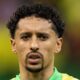 Marquinhos, jogador de futebol, com camisa verde e amarela, cabelo crespo e olhar sério.