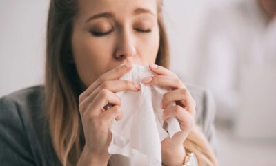 Mulher com olhos fechados segura lenço de papel branco no nariz, indicando espirro ou resfriado.