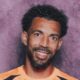 Retrato de Josimar Dias, o Vozinha, sorrindo com cabelo crespo, barba e camisa laranja.