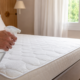 O vinagre no colchão virou um daqueles truques domésticos que chamam atenção pela simplicidade. Como passamos muitas horas em contato direto com a cama, é normal que o tecido acumule suor, umidade, odores e resíduos que nem sempre aparecem na limpeza do dia a dia. A ideia não é encharcar nem substituir uma higienização profunda, mas usar o vinagre branco com cuidado para ajudar a neutralizar cheiros e deixar a superfície mais fresca antes de colocar a roupa de cama novamente. Por que rociar vinagre no colchão pode funcionar? O vinagre branco é conhecido na limpeza doméstica por causa do ácido acético, substância que ajuda a reduzir odores e pode dificultar a permanência de alguns microrganismos em superfícies. No colchão, o maior benefício costuma ser a sensação de frescor depois que o tecido seca completamente. Esse cuidado é útil especialmente quando há cheiro de suor, ambiente pouco ventilado ou sensação de colchão abafado. Ainda assim, o segredo está na quantidade: a aplicação deve ser leve, sem molhar demais a espuma ou deixar a superfície úmida por muito tempo. Quais benefícios o vinagre pode trazer para a cama? Quando usado corretamente, o vinagre atua como um reforço simples na limpeza do colchão. Ele não faz milagre, mas pode melhorar o conforto entre lavagens de lençóis, trocas de protetores e limpezas mais completas. Os principais efeitos aparecem no controle de odores e na manutenção da superfície onde você dorme todos os dias: ajuda a reduzir cheiro de suor no colchão; contribui para neutralizar o odor de umidade; refresca o tecido sem perfume forte; pode complementar a rotina contra ácaros no colchão; é uma alternativa simples para a limpeza natural da casa. Quando o vinagre ajuda mais Situações em que o truque faz sentido 🛏️ Casa limpa 💨 Cheiro abafado Ajuda a suavizar odores acumulados pelo uso diário e pela pouca ventilação. 🌬️ Quarto ventilado Funciona melhor quando o colchão seca ao ar livre ou perto de uma janela aberta. ✨ Manutenção leve É indicado como cuidado complementar, não como substituto da higienização profunda. Como usar vinagre no colchão sem estragar? Para aplicar com segurança, retire lençóis, fronhas, capas e protetores. Coloque o vinagre em um borrifador limpo e espalhe uma névoa fina sobre a superfície, evitando deixar áreas encharcadas. O objetivo é umedecer de leve, não molhar a parte interna do colchão. Depois, deixe agir por alguns minutos e permita que o tecido seque totalmente em local ventilado. Se possível, abra janelas, ligue um ventilador ou deixe o colchão receber luz natural indireta. Só arrume a cama quando não houver mais umidade ao toque. Quais cuidados evitam mau cheiro no colchão? O vinagre ajuda, mas a prevenção continua sendo o melhor caminho. Trocar a roupa de cama com frequência, usar protetor lavável e manter o quarto arejado reduz a umidade acumulada e melhora a sensação de limpeza por mais tempo. Também vale aspirar a superfície do colchão antes da aplicação, principalmente em casas com pets, poeira ou alergias. Esse hábito remove partículas soltas e deixa o cuidado mais eficiente, sem depender apenas de soluções líquidas. Quando não vale usar vinagre no colchão? Evite o truque se o colchão estiver muito molhado, com mofo visível, manchas profundas ou cheiro persistente que não melhora com ventilação. Nesses casos, insistir no vinagre pode mascarar o problema por pouco tempo e atrasar uma limpeza adequada. Também não misture vinagre com produtos químicos, água sanitária ou desinfetantes fortes. Para manter a cama segura, use o método com moderação, teste em uma pequena área e priorize sempre a secagem completa antes de dormir.