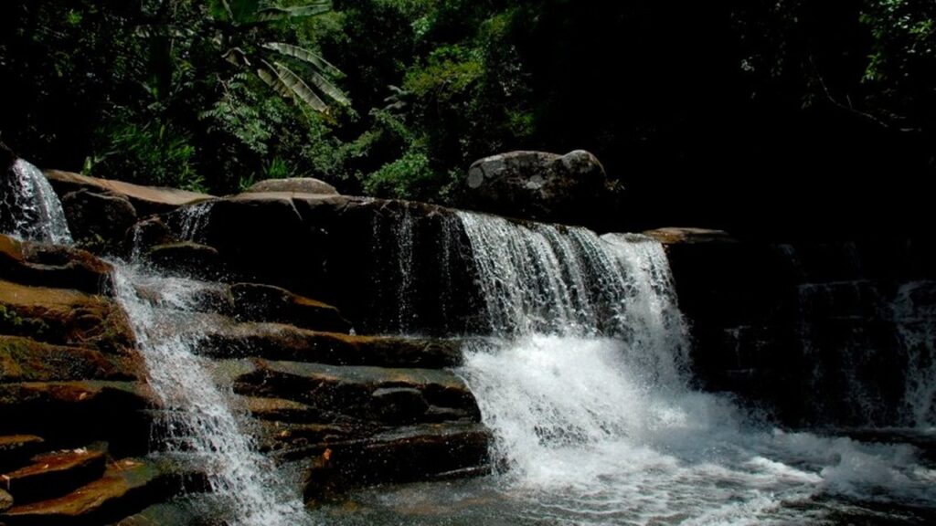 Cascata de múltiplas quedas sobre rochas escuras em meio à vegetação verde exuberante.