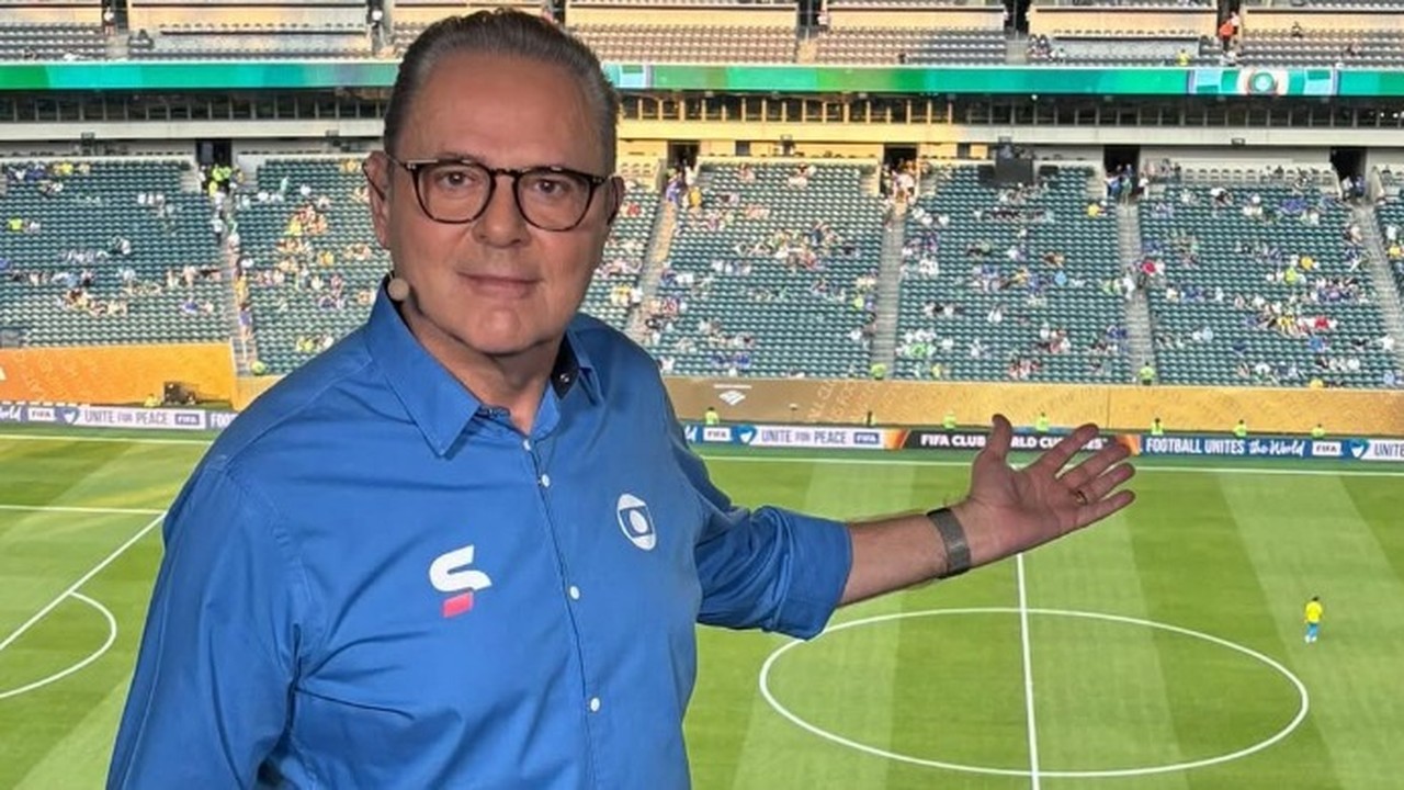 Luís Roberto de óculos e camisa azul da Globo gesticula em estádio de futebol.
