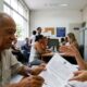 Homem idoso e mulher em mesa de cartório examinando documentos com uma caneta.