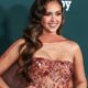 Jessica Alba sorri, cabelo castanho ondulado, vestido brilhante, fundo verde com logo 'Baby 2 Baby'.