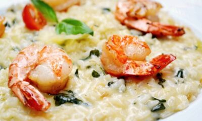 Risoto de camarão cremoso em prato branco com camarões inteiros, manjericão e tomate cereja.
