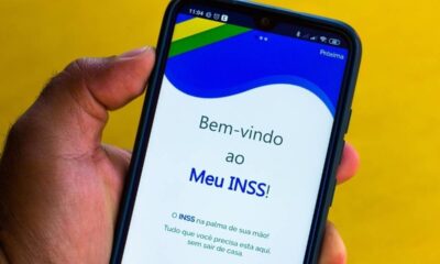 Mão segura smartphone com aplicativo Meu INSS aberto, exibindo 'Bem-vindo ao Meu INSS!' na tela.