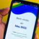 Mão segura smartphone com aplicativo Meu INSS aberto, exibindo 'Bem-vindo ao Meu INSS!' na tela.