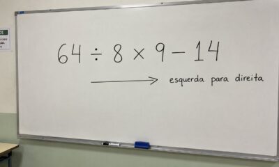 Quadro branco realista em uma sala de aula simples com a expressão “64 ÷ 8 × 9 − 14” escrita em destaque e, abaixo, uma seta apontando para a direita com a anotação “esquerda para direita”, sem mostrar o resultado.