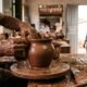 Mãos de artesão moldando um vaso de barro em roda de oleiro, com observadores ao fundo.