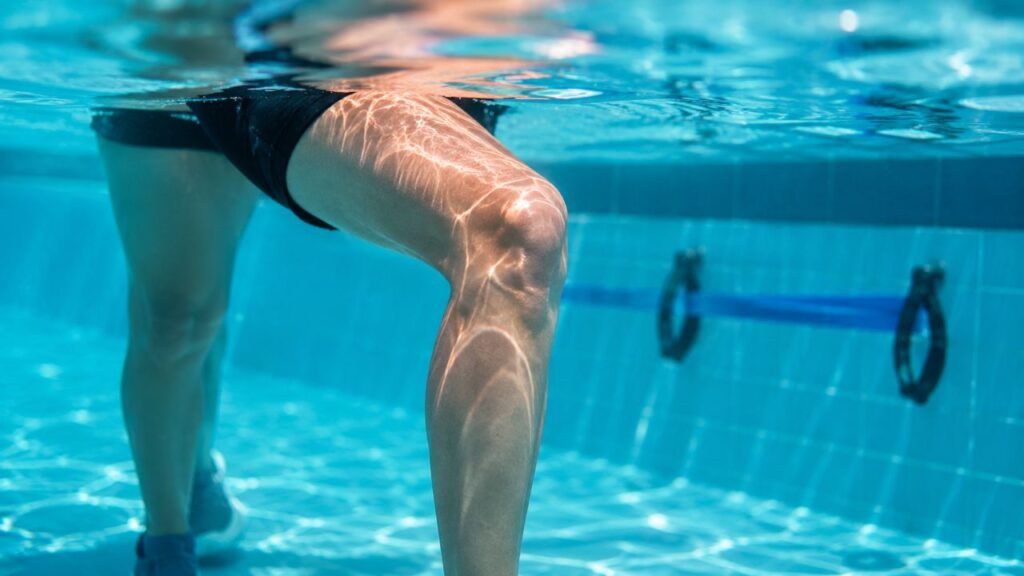 Joelho parcialmente submerso em piscina durante exercício aquático de baixo impacto.