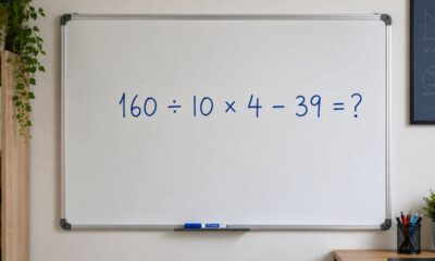 Quadro branco em sala de estudo limpa com o cálculo “160 ÷ 10 × 4 − 39 = ?” escrito em azul e um marcador sobre a bandeja inferior.
