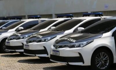 Viaturas da Polícia Civil, brancas e pretas, com luzes azuis no teto, estacionadas