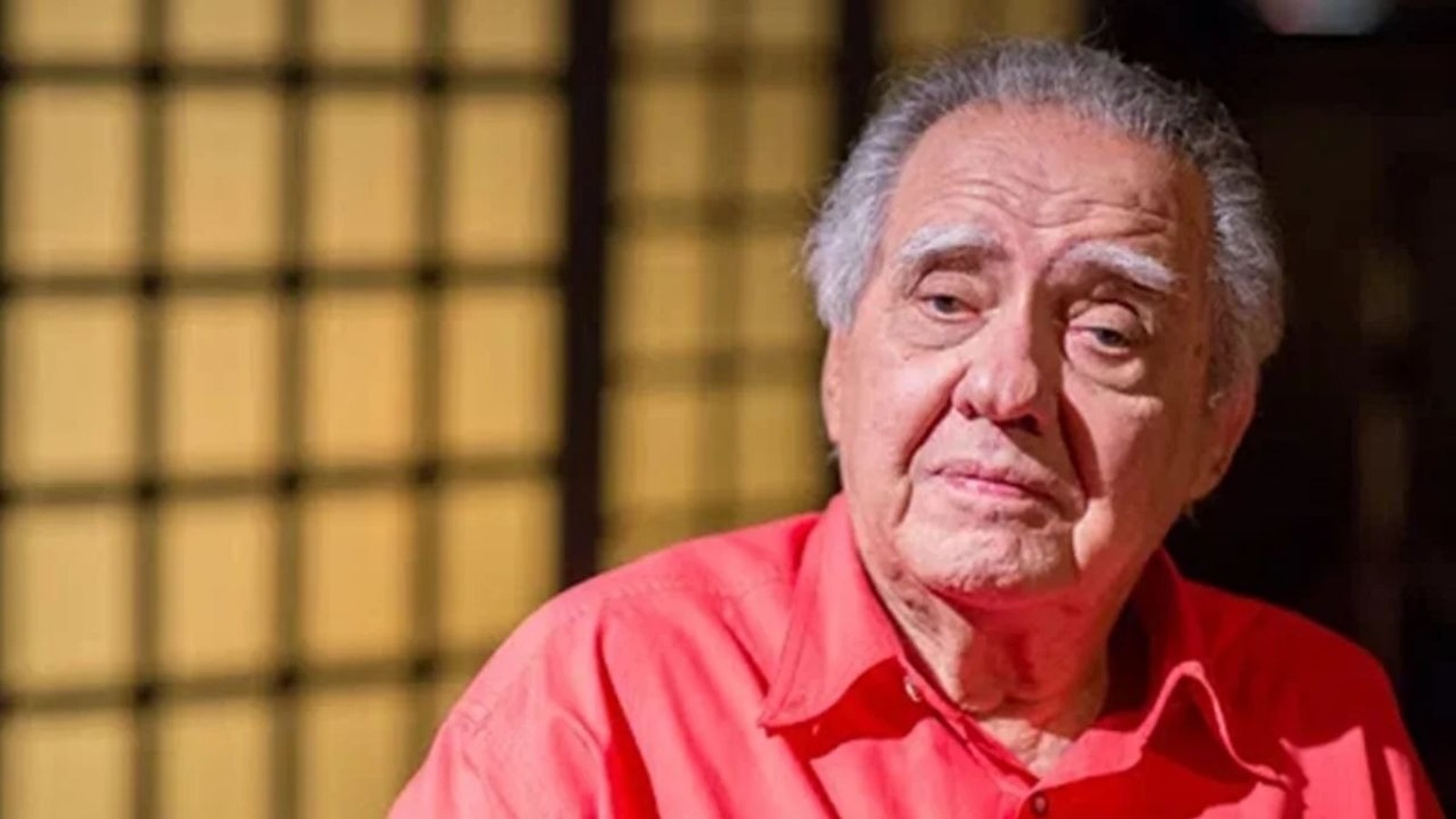 Luiz Carlos Barreto, homem idoso com cabelo grisalho e camisa vermelha, olhando pensativo
