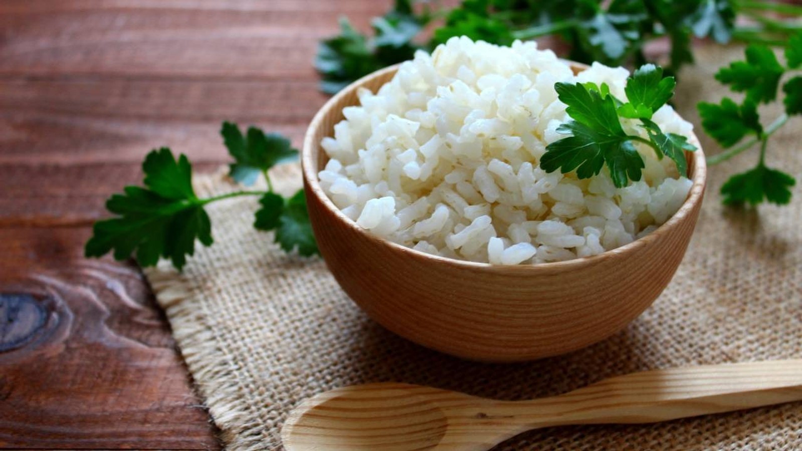 Tigela de madeira com arroz branco soltinho, salsa e colher de madeira