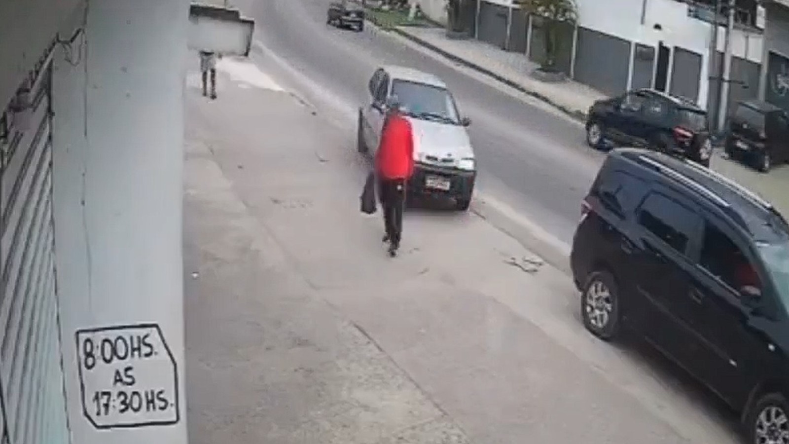 Homem em vermelho na calçada, carro prateado ao lado. Poste com sinal "8:00HS. AS 17:30HS".