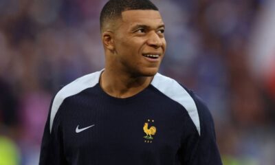 Kylian Mbappé sorrindo, vestindo a camisa azul da França com o logo Nike e emblema FFF.