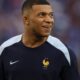 Kylian Mbappé sorrindo, vestindo a camisa azul da França com o logo Nike e emblema FFF.