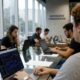 Grupo de pessoas trabalha em laptops, um com gráficos financeiros, em escritório com 'Inovações Financeiras' na parede