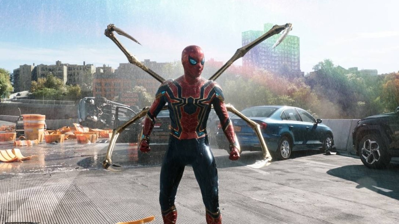 Homem-Aranha com traje vermelho e dourado, braços mecânicos, em rodovia destruída e chuvosa.