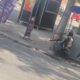 Dois homens em coletes táticos e fuzis, agachados atrás de postes em rua urbana