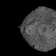 Asteroide Bennu cinza irregular com superfície rochosa e granular no espaço escuro