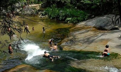 Pessoas nadam e escorregam em um rio com poços e rochas em área de mata