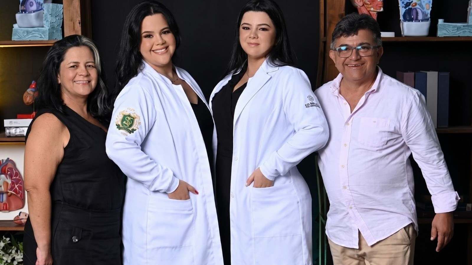 Quatro pessoas, mãe, pai e duas filhas de jaleco branco, sorrindo para a câmera