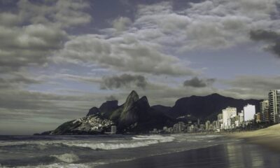 Praia com ondas, prédios da cidade e montanhas sob céu nublado no Rio de Janeiro