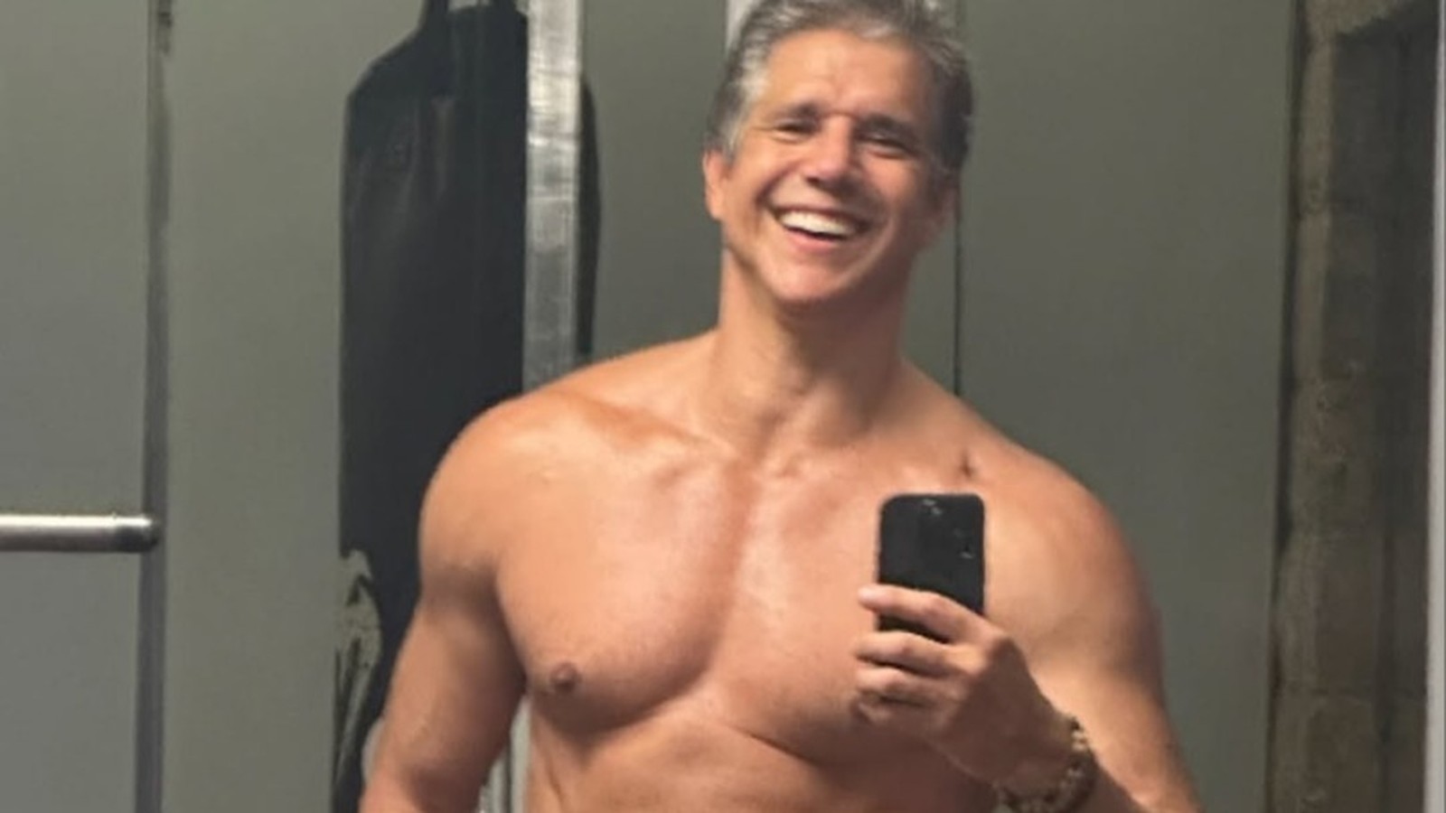 Márcio Garcia sorri, sem camisa, tira selfie no espelho, exibindo físico musculoso e cabelo grisalho.