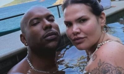 Homem careca e mulher com tatuagens submersos em piscina, olhando para câmera