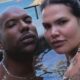 Homem careca e mulher com tatuagens submersos em piscina, olhando para câmera