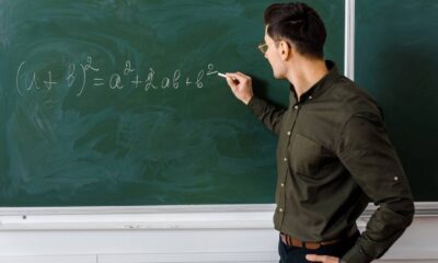 Homem escreve equação (a + b)² = a² + 2ab + b² com giz em quadro-negro verde
