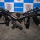 Dois fuzis, um com "QUITUNGO" no corpo, uma pistola e rádio em chão de concreto, fundo PMERJ