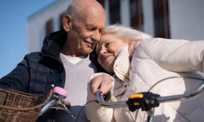 Casal de idosos abraçado com carinho ao lado de uma bicicleta com cesta, sob céu azul
