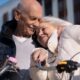 Casal de idosos abraçado com carinho ao lado de uma bicicleta com cesta, sob céu azul