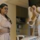 Mulher de pijama observa profissional de saúde com máscara mostrando bolsa de colostomia em quarto